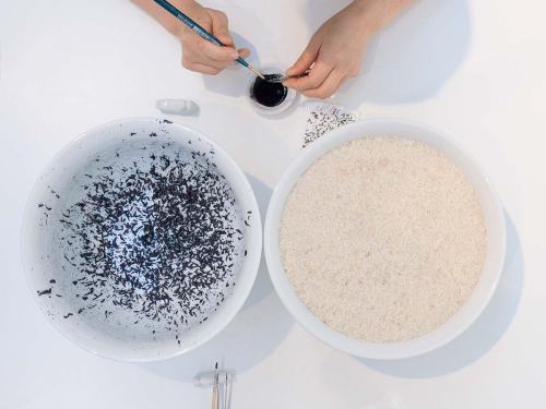 Chun Hua Catherine Dong paints rice with black ink one after one and invites audiences to sit in front of her and paint the rice with her